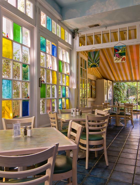 Large dining area with tiled flooring, light wooden tables and chairs, and large stained glass windows