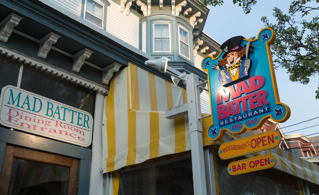 Close up view of Mad Batter Restaurant signs next to yellow and white striped outdoor patio canopy