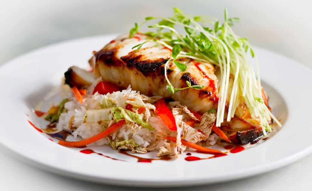 Close up view of a grilled fish dish with rice and sprouts on a white plate