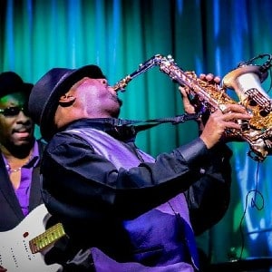 A group of musicians playing a variety of jazz instruments under yellow stage lights