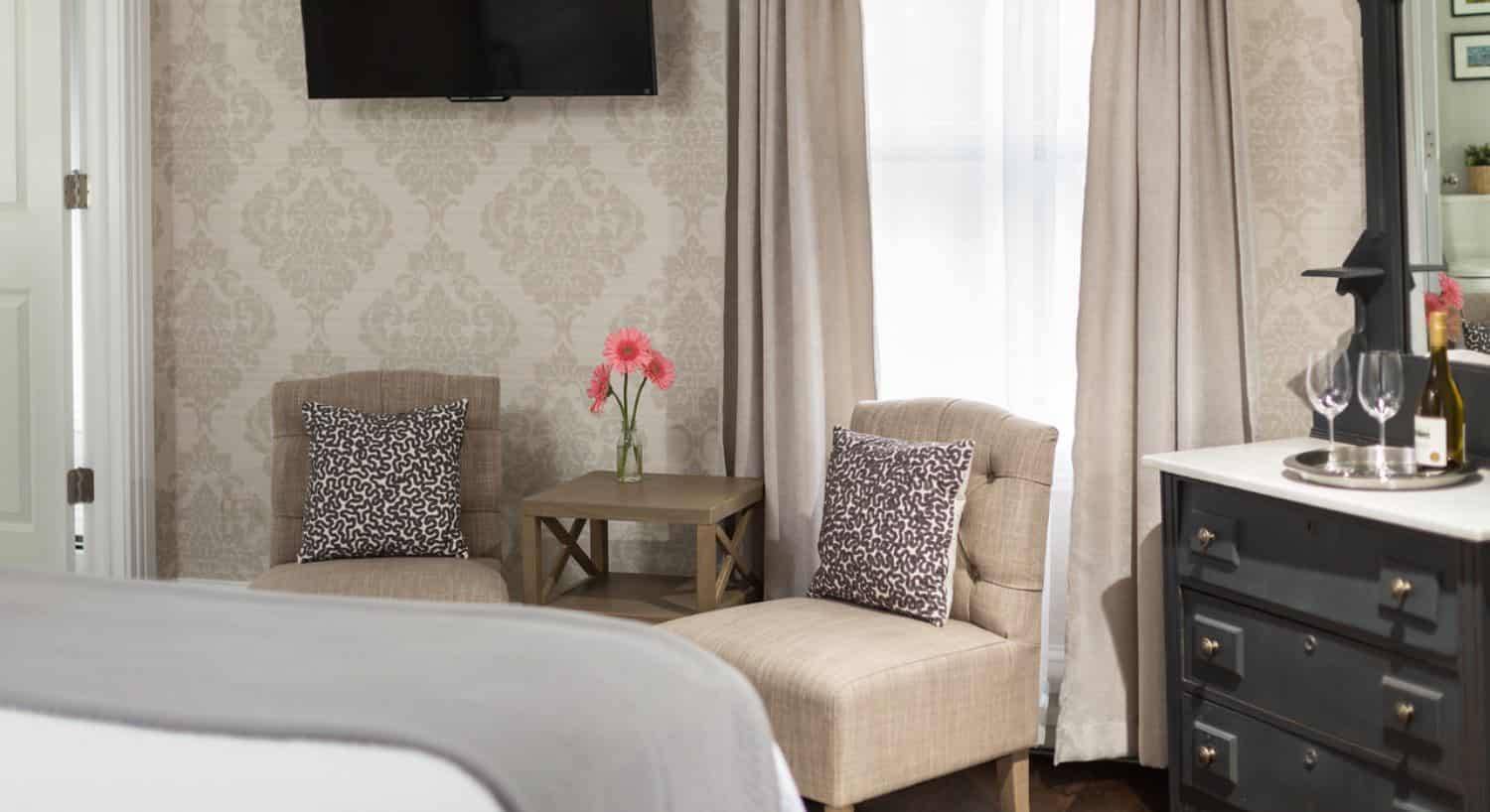 Bedroom with sitting area including two upholstered chairs, flat-screen TV, and dark wooden dresser with marble top and mirror