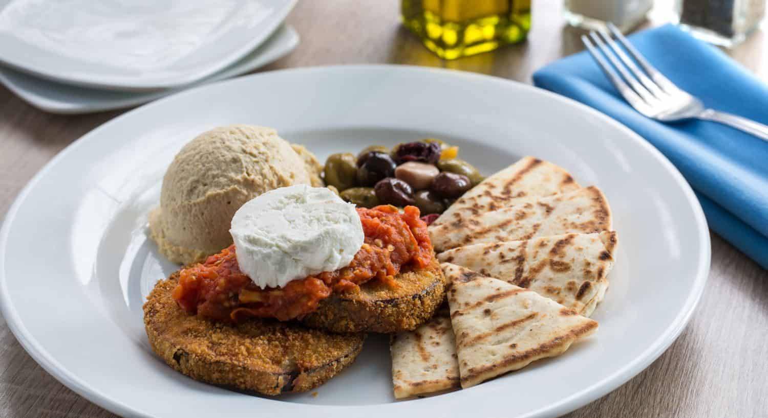 Close up view of a mediteranean dish with humus, olives, and pita bread on a white porcelain plate