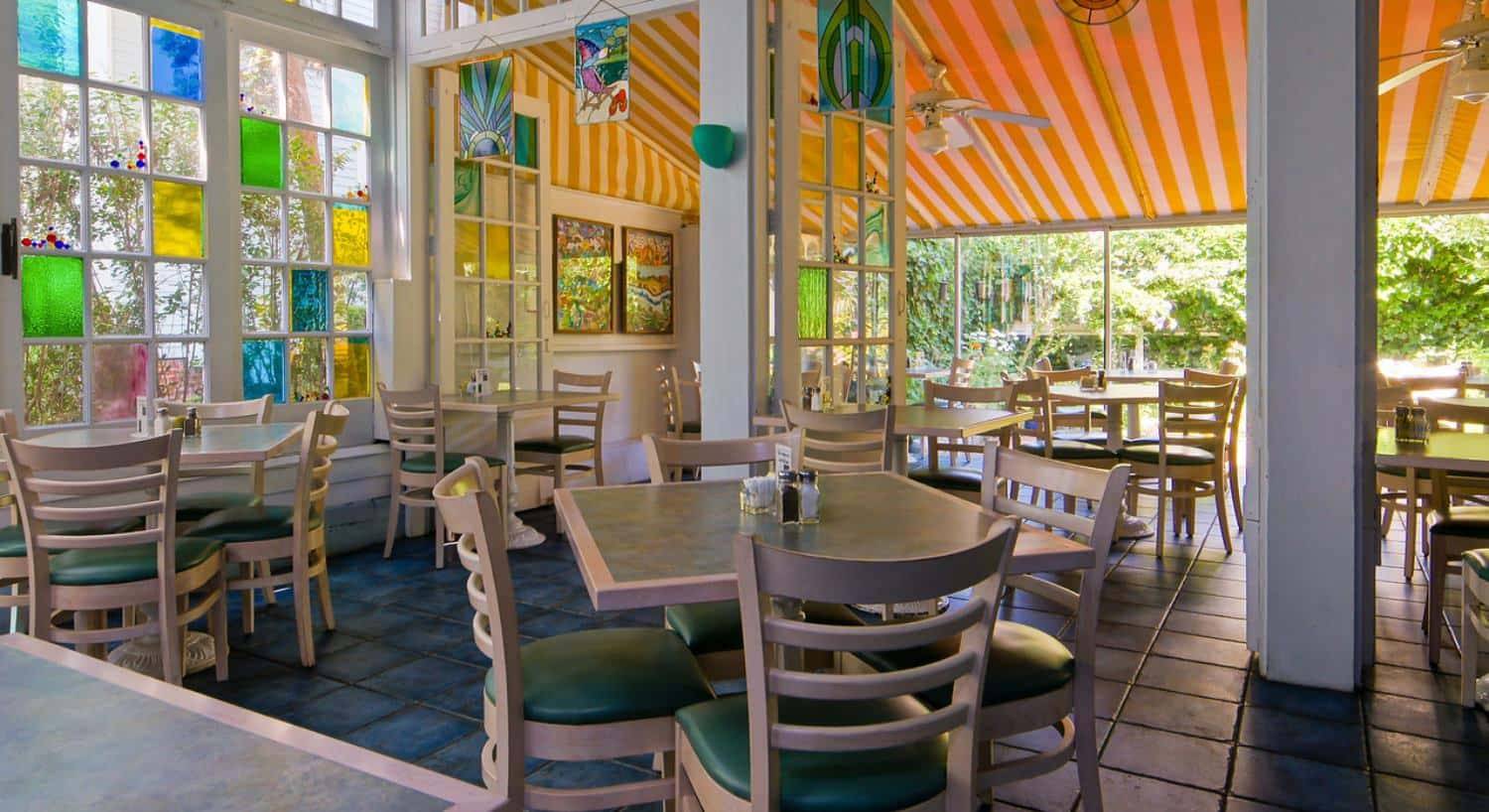 Large dining area with tiled flooring, light wooden tables and chairs, and large stained glass windows