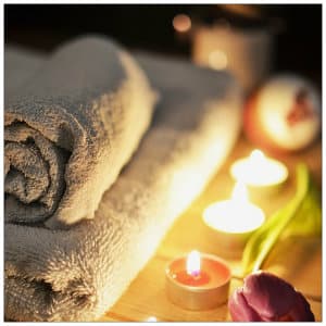Two rolled towels next to pink lit candles and a fresh flower on a brown table 