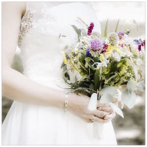 Bride standing in a white wedding dress with a lace top holding a spring bouquet of flowers
