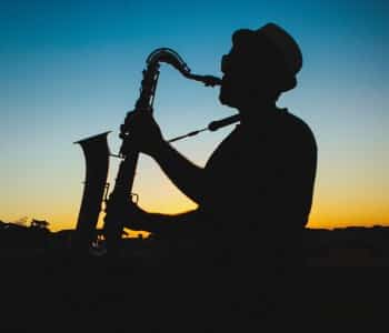 Silhouette of a man wearing a hat playing a saxophone at sunset