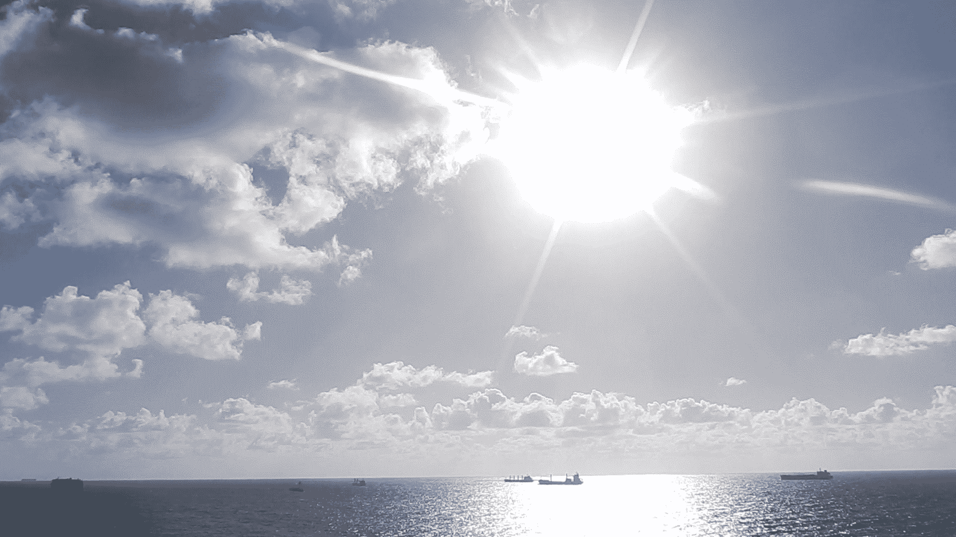Sunshine glittering on the ocean surface amidst puffy white clouds