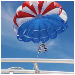 Red, white and blue parasail flying in the air above a white boat - image by aj-garcia-www.unsplash.com