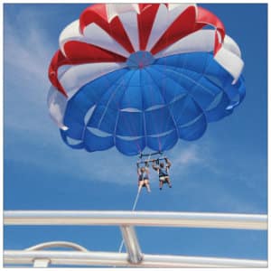 Red, white and blue parasail flying in the air above a white boat - image by aj-garcia-www.unsplash.com