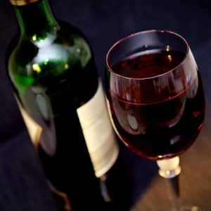 A green bottle of wine next to a tall glass full of red wine